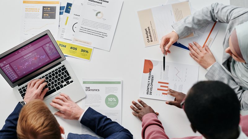 A team reviewing printed annual reports, charts and financial statements around a table