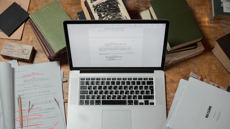 A printed manuscript marked with red editing notes beside a laptop, representing book editing