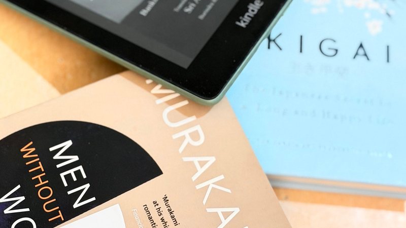 A Kindle e-reader beside printed book covers, representing ebook versus print cover design